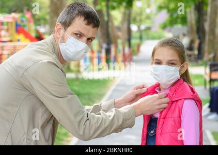 Papa auf der Straße setzt seine Töchter vor eine medizinische Maske, in den Rahmen geschaut Stockfoto