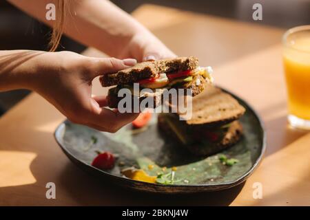 Frau in Händen halten gebissene Sandwich. Roggen geröstet Brot mit Avocado. Frischer Orangensaft Vegane Speisen Stockfoto