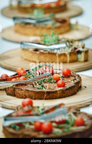 Die Pasteten mit Kirschtomaten und grünen Keimen liegen auf runden Holzschalen und in Scheiben mit Zange geschnitten Stockfoto