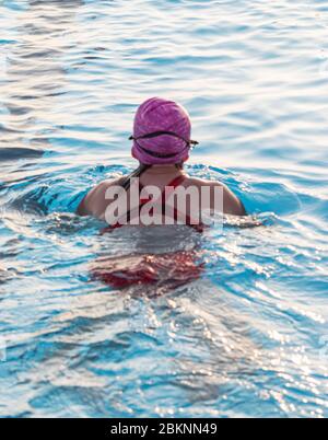 Rückansicht einer Schwimmerin, die eine rosa Mütze und eine rote Badesuite trägt. Stockfoto