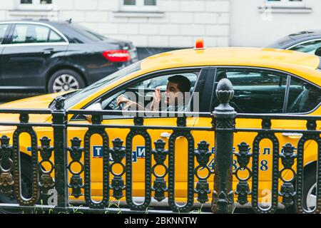 Moskau, Russland - 7. JULI 2017: Taxifahrer sitzt in einem gelben Auto vor dem Hintergrund von Verkehr und anderen Autos und er raucht im Auto Stockfoto