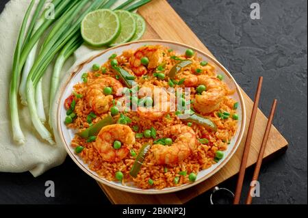 Thai Tom Yum gebratener Reis oder Prawn Biryani in weißem Teller auf schwarzem Schiefer Hintergrund. Tom Yum Fried Rice ist Thailand Küche Gericht mit Jasminreis, Garnelen Stockfoto