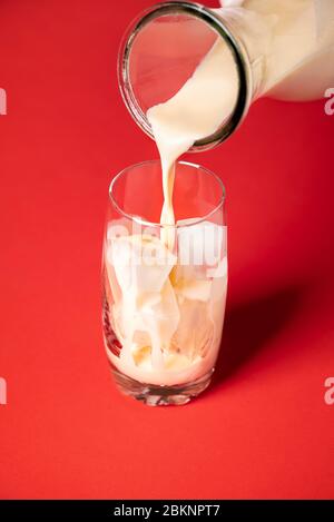 Horchata Mocktail Kontext erstellen. Horchata-Milch in ein Glas mit Eiswürfeln auf rotem Grund gießen. Mexikanischer Sommerdrink. Hausgemachtes Getränk Stockfoto