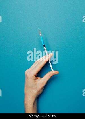 Hand hält Spritze mit experimentellem Coronavirus-Impfstoff auf blauem Hintergrund, Draufsicht. Medizin Medizin Impfung Coronavirus Covid-19 Konzept Stockfoto