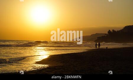 Ein paar Leute an einem Strand mit einem Sonnenuntergang im Hintergrund. In EL Zonte, El Salvador Stockfoto