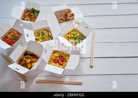 Verschiedene orientalische Gerichte verpackt in Papierkarton. Das Essen wird auf dem Tisch geliefert. Asiatisches Take Away-Konzept Stockfoto