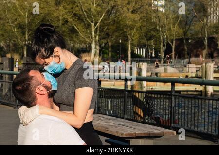 Ein Paar genießt das warme Wetter während der COVID-19 Coronavirus Pandemie und trägt Schutzmaske und Handschuhe im Battery Park. Stockfoto