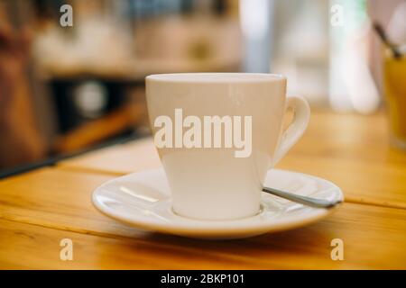 Weiße Tasse mit Kaffee auf einem Teller. Heißer Espresso in einer Tasse auf einem Holztisch. Espresso zum Frühstück in einem Café Stockfoto