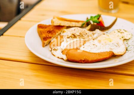 Hilfreiches appetitliches Frühstück auf einem weißen Teller. Rührei mit Gemüse und Croutons in einem Café. Frühstück im Café: Rührei, Würstchen Stockfoto