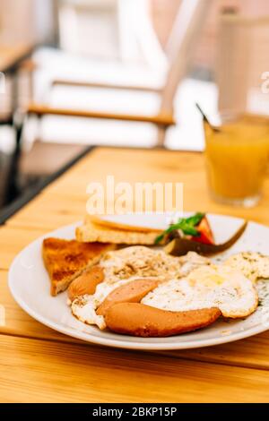 Hilfreiches appetitliches Frühstück auf einem weißen Teller. Rührei mit Gemüse und Croutons in einem Café. Frühstück im Café: Rührei, Würstchen Stockfoto