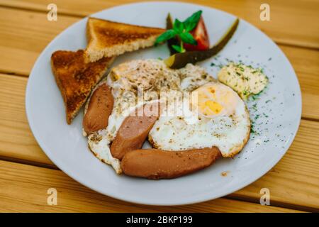 Zum Frühstück Spiegeleier mit Tomaten, Gurken und Käse. Rührei mit Würstchen und Tomaten in einem Café. Reichhaltiges Frühstück mit Eiern, Stockfoto