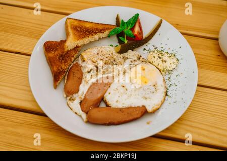 Zum Frühstück Spiegeleier mit Tomaten, Gurken und Käse. Rührei mit Würstchen und Tomaten in einem Café. Reichhaltiges Frühstück mit Eiern, Stockfoto