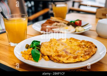 Frühstück im Café: Omelette mit Würstchen, Toast und ein Glas frischen Saft. Leckeres Omelett mit Schinken und Erbsen zum Garnieren. Omelette und ein Glas Stockfoto