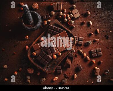 Kakaopulver, Bohnen und Schokoriegel Stücke auf dunklem Holzhintergrund. Stockfoto