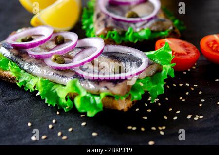 Appetitliches Smorrebrod mit norwegischem Hering, Salat, blauer Zwiebel, Zitrone und Tomate liegt auf einem Holzbrett Stockfoto