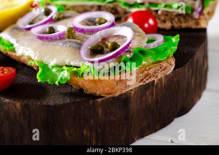 Appetitliches Smorrebrod mit norwegischem Hering, Salat, blauer Zwiebel, Zitrone und Tomate liegt auf einem Holzbrett Stockfoto