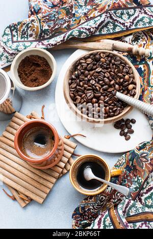 Blick von oben auf eine Schüssel mit Kaffeebohnen, neben gemahlenem Kaffee, eine Tasse Kaffee und einen gemusterten Schal. Stockfoto
