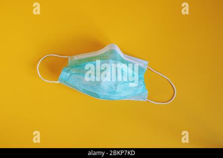 Medizinische oder chirurgische Maske - gebrauchte Einweg-Schutzmaske auf gelbem Hintergrund Stockfoto