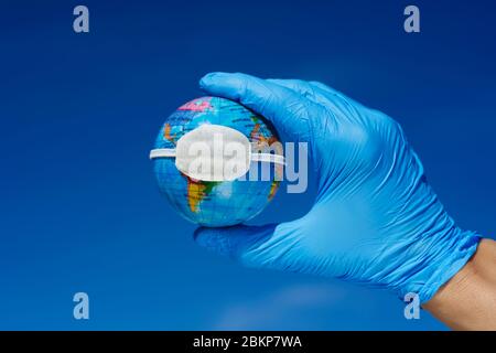 Nahaufnahme eines Mannes, der blaue Operationshandschuhe trägt, einen Erdglobus mit einer Schutzmaske hält, der die globale Coronavirus-Pandemie oder das A darstellt Stockfoto