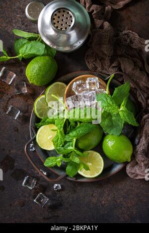 Erfrischende Mojito-Cocktailzubereitung. Minze, Limette, Eiszutaten und Barutensilien auf dunklem Steingrund. Draufsicht flach legen Hintergrund. Stockfoto