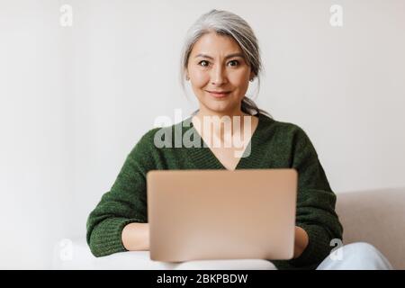 Bild von schönen Erwachsenen asiatische Frau mit Laptop-Computer während auf dem Sofa zu Hause sitzen Stockfoto