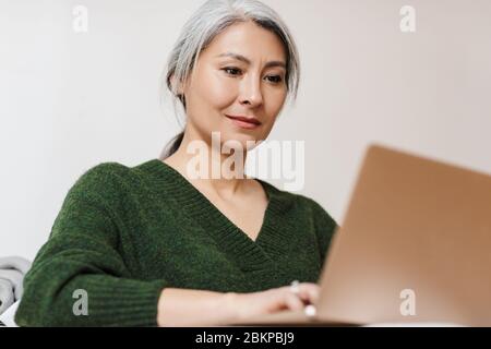 Bild von schönen Erwachsenen asiatische Frau mit Laptop-Computer während auf dem Sofa zu Hause sitzen Stockfoto