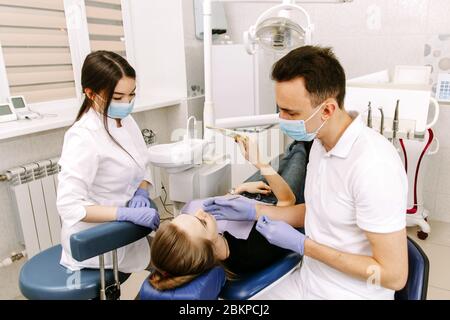 Eine junge Frau liegt auf dem Zahnarztstuhl. Der Patient bewertet die Arbeit des Zahnarztes mit einem Spiegel. Stockfoto