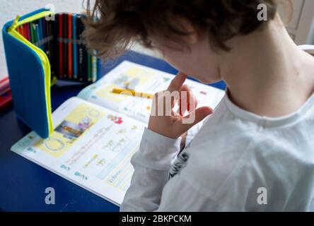 Erstklaessler (7 Jahre) sitzt zu Hause an einem Tisch und erledigt deutsche Aufgaben in seinem Booklet "Alphabet Booklet - BASIC Font", am 4. Mai 2020 in Mülheim an der Ruhr. ¬ Verwendung weltweit Stockfoto