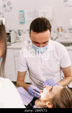 Eine schöne Frau liegt im Zahnarztstuhl. Der Arzt und der Assistent behandeln die Zähne des Patienten. Werbung leer. Stockfoto