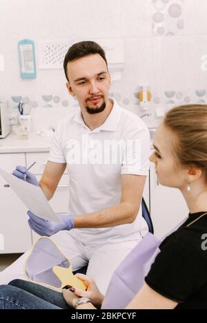 Ein schönes Mädchen sitzt im Zahnarztstuhl und hört dem Arzt zu. Zahnarzt Termin und zahnärztliche Versorgung. Stockfoto