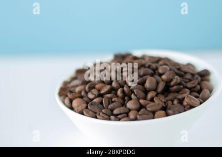 Geröstete Kaffeebohnen in einer weißen Schüssel mit himmelblauem Hintergrund Stockfoto