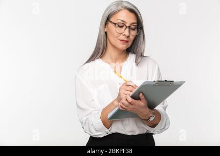 Porträt einer attraktiven nachdenklichen reifen Geschäftsfrau in formeller Kleidung, die isoliert auf weißem Hintergrund steht und ein Klemmbrett hält Stockfoto
