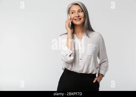 Porträt einer attraktiven lächelnden reifen Geschäftsfrau in formeller Kleidung stehend isoliert auf weißem Hintergrund, im Gespräch auf dem Handy Stockfoto