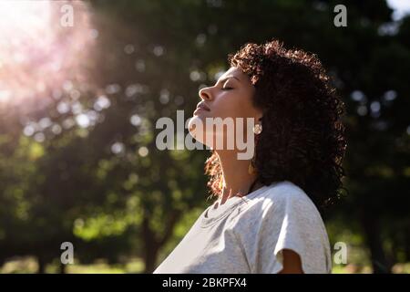 Junge Frau im Freien, die die Sonne auf ihrem Gesicht fühlt Stockfoto