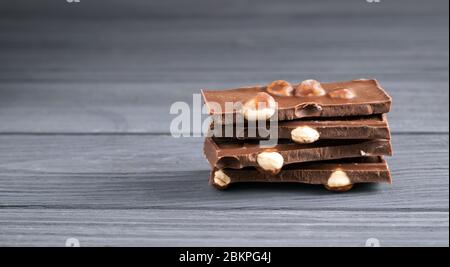 Stapel von Milchschokoladenstücken mit Nüssen auf grauem Holztisch. Stapel von Schokoriegel Schokoladenstücke mit großen Haselnuss Stockfoto