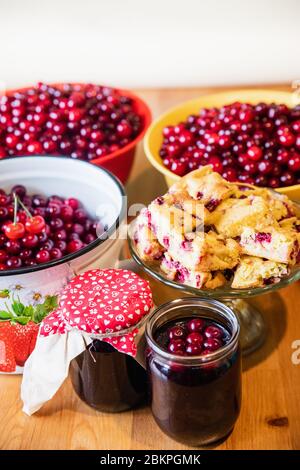 Gläser von leckeren Sommer Kirsche Marmelade mit gebackenen Kirsche Kuchen und rohe Kirschen Hintergrund Stockfoto