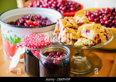 Gläser von leckeren Sommer Kirsche Marmelade mit gebackenen Kirsche Kuchen und rohe Kirschen Hintergrund Stockfoto