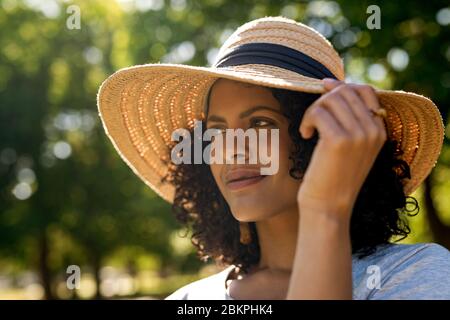 Junge Frau, die in einem Park steht und einen Sonnenhut trägt Stockfoto