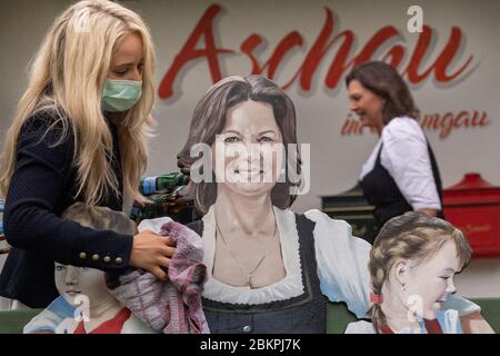 Aschau Im Chiemgau, Deutschland. Mai 2020. Stefanie Sattlberger (l), Tourismus- und Freizeitkauffrau, wischt das neu gemalte Porträt von Ilse Aigner (CSU), Präsidentin des Bayerischen landtags, für eine Fotosession mit einem Handtuch trocken. 2014 schenkte Ilse Aigner (im Hintergrund rechts) die Bank mit dem Namen 'Ilse's Lausdirndlbankerl' dem Dorf Aschau im Chiemgau, auch bekannt als 'Bankerldorf'. Der Politiker war damals Bayerischer Wirtschaftsminister. Quelle: Peter Kneffel/dpa/Alamy Live News Stockfoto