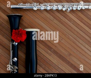 Oboe, Klarinette und Flöte auf einer Holztafel mit roter Blume. Stockfoto