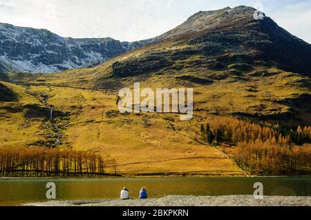 Wanderer, die am Ufer von Buttermere im Lake District sitzen, mit Burtness Comb, Eagle Crag und High Stile dahinter Stockfoto