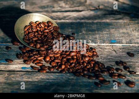 Kaffeebohnen in altem kleinen Silber mit dem rustikalen blauen Holzhintergrund mit Sonnenlicht darauf. Stockfoto