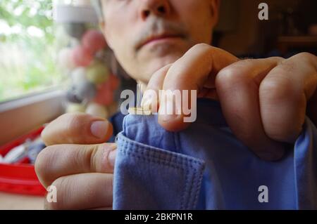 Schneidermann mit Nadel und Faden in der Hand. Handgefertigte Arbeit. Manuelles Nähen auf den Hemdknopf. Heimwerkerhandwerk. Stockfoto