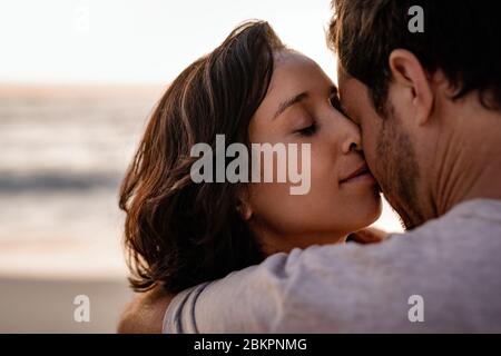 Liebevolle Frau, die in den Armen ihres Mannes an einem Strand steht Stockfoto