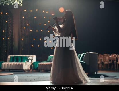 Mädchen in weißem Kleid spielt Violine auf der Bühne. Stockfoto