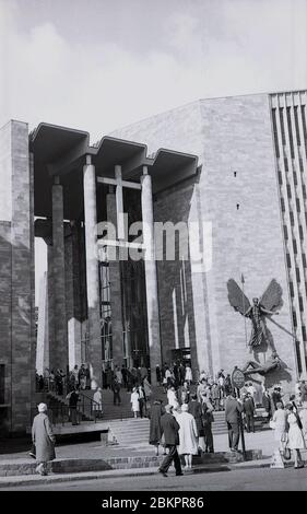 1961, historisches Bild von Menschen vor der neuen Kathedrale, Coventry, England bei ihrer offiziellen Eröffnung. Im Mai 1962 wurde im Zweiten Weltkrieg schwer bombardiert und an der Stelle der Ruinen der alten Kathedrale wurde ein neues "modernistisches" Bauwerk errichtet. Der radikale Entwurf wurde von Basil Spence im "Brutalistischen" Architekturstil entworfen, der in dieser Zeit üblich war. Stockfoto