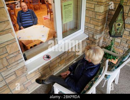 Balve, Deutschland. Mai 2020. Engelbert Prumbaum winkt seiner Tochter Andrea Rapp aus dem Fenster des St. Johannes-Altenheim. Während er hinter einer Plexiglasscheibe in der ungenutzten Cafeteria der Anlage sitzt, hat sie sich draußen auf einem Stuhl gesetzt. Alte Menschen- und Pflegeheime in NRW tun viel, um auch bei der Corona-Pandemie Verwandten einen Besuch zu ermöglichen. Quelle: Bernd Thissen/dpa/Alamy Live News Stockfoto