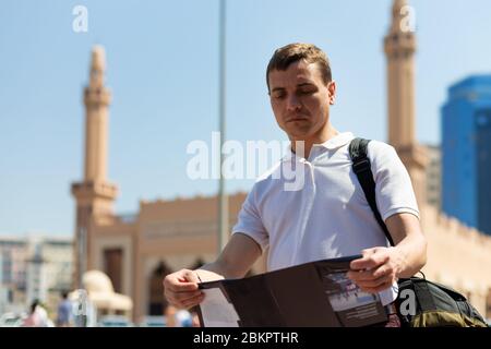 Ein 35-40-jähriger Tourist mit einer Karte in den Händen steht vor der Kulisse einer islamischen Moschee, Stockfoto