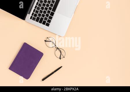 Draufsicht auf Laptop, Brille und Schreibwaren auf beigefarbenem Hintergrund. Fernlernkonzept mit Kopierraum. Stockfoto