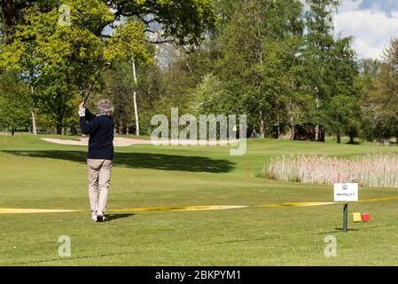 05. Mai 2020, Hamburg: Ein Mann schlägt auf dem abgekürzten Abschlag A2 auf dem Gelände des Golfclubs Hamburg-Wendlohe hinter einem Sperrband auf der Schleswig-holsteinischen Seite des Golfclubs einen Ball. Der Abschlag ist in Schleswig-Holstein, das Grün in Schleswig-Holstein, aber auf dem Weg dorthin ist Hamburg-Gebiet: Diese Konstellation auf dem A2-Platz des Golfclubs Hamburg-Wendlohe stellt den Spielern derzeit eine ganz besondere Herausforderung dar. In Schleswig-Holstein ist das Golfen seit Montag wieder erlaubt, in Hamburg aber noch nicht aufgrund von Corona-Bedingungen. Das Problem wurde auf der Wendlohe geschickt gelöst. Stockfoto